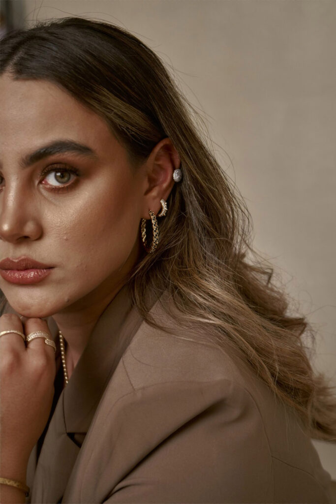 Valeria Cisneros a model with a striking appearance showcases her earrings and jewelry set against a neutral backdrop.